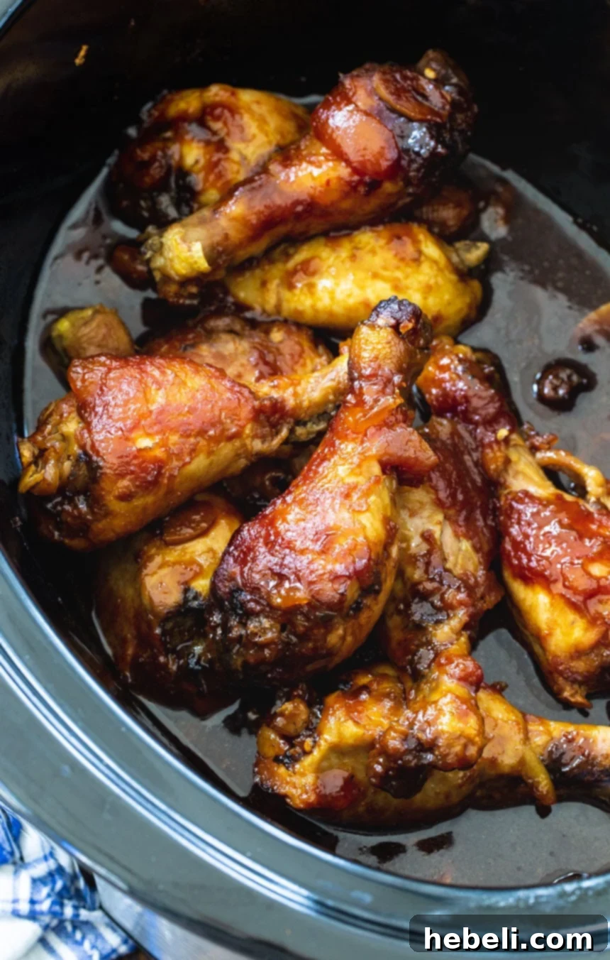 Chicken Legs simmering in a black slow cooker, covered in a rich, glossy peach glaze.