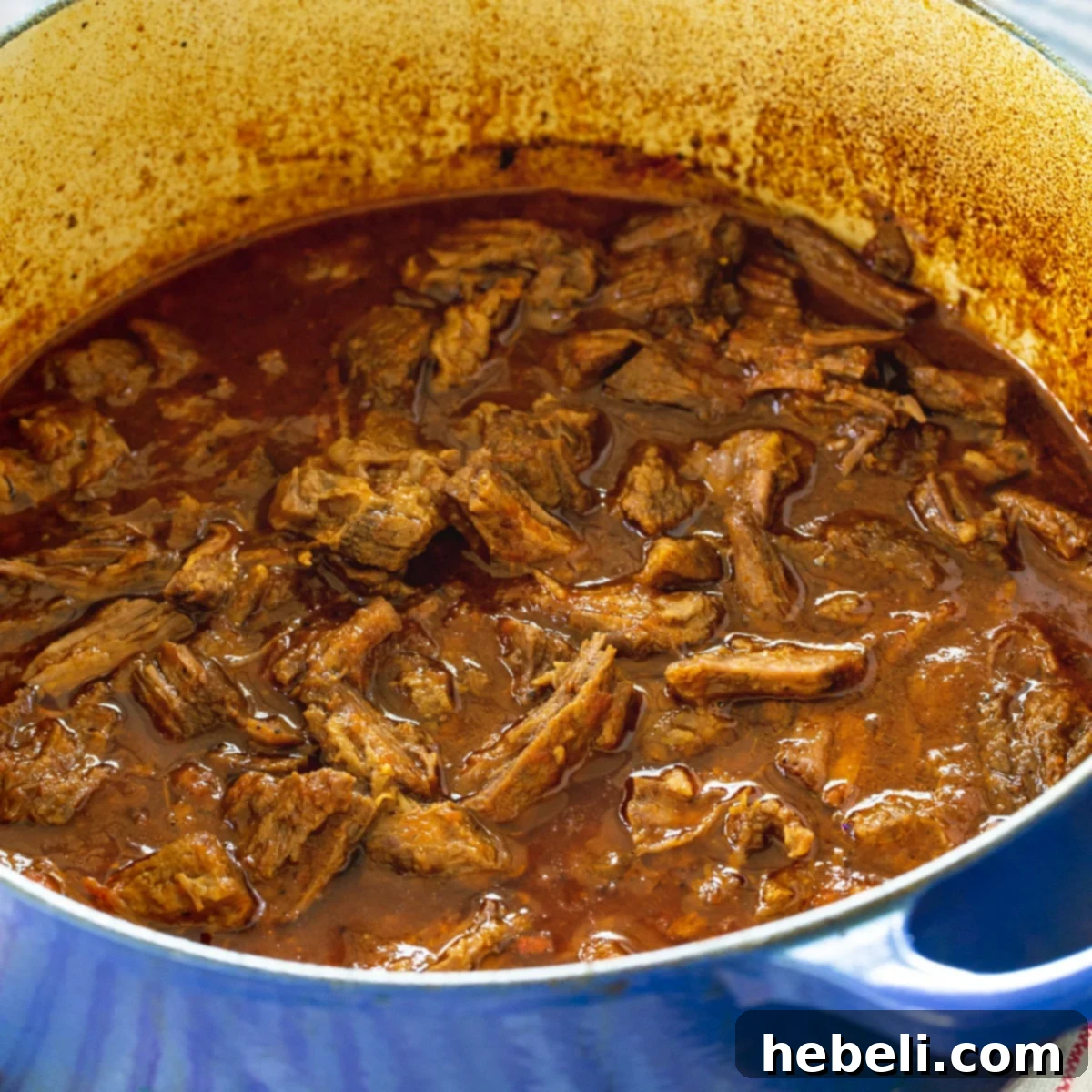 Sweet and Tangy Barbecue Beef, slow-cooked to perfection in a rustic Dutch oven, highlighting its rich, glossy sauce and tender shredded texture. Ideal for a hearty family meal.