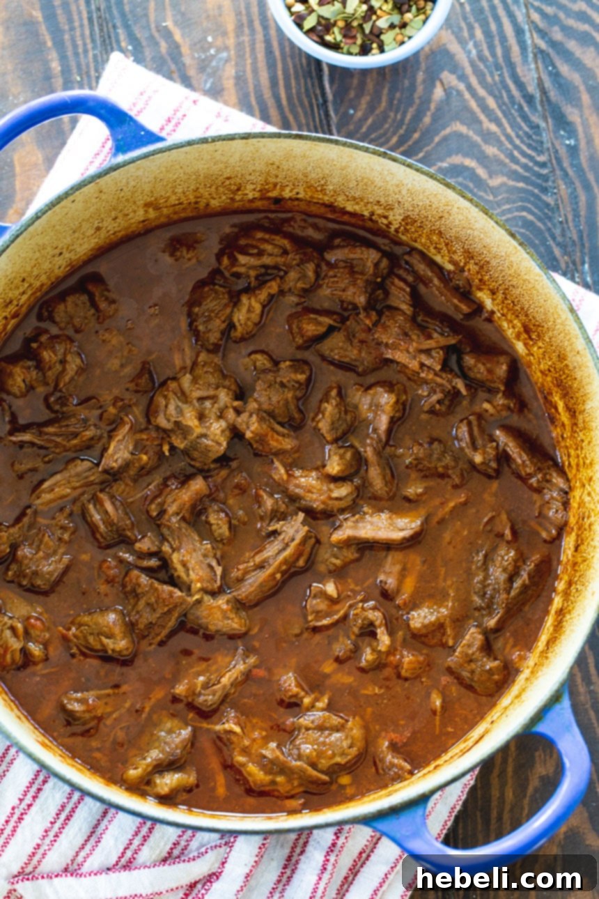 Sweet and Tangy BBQ Beef in a vibrant blue Dutch oven, showcasing its rich, deep color and succulent texture as it simmers to perfection.
