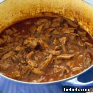BBQ Beef in a Dutch oven, featuring tender, shredded meat in a rich, dark sauce, ready to be dished out.