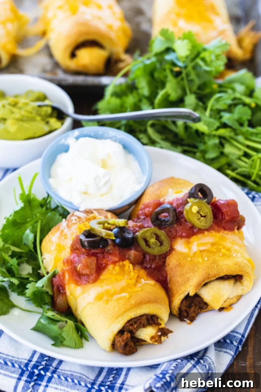 Two freshly baked Crescent Beef Burritos on a plate, garnished with vibrant fresh cilantro and a dollop of sour cream, ready for a delicious meal.