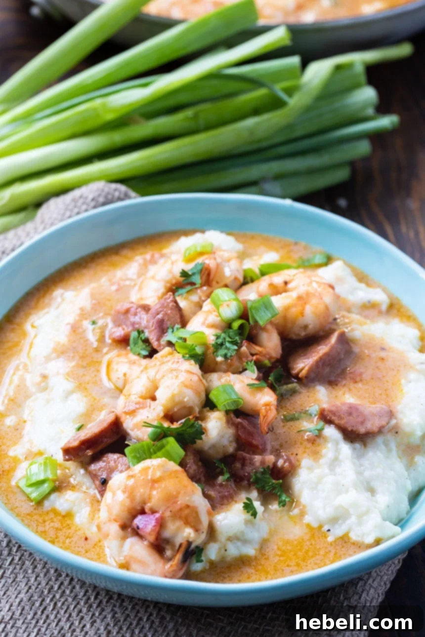 A close-up view of Smothered Shrimp and Parmesan Grits in a blue bowl, garnished with fresh green onions.