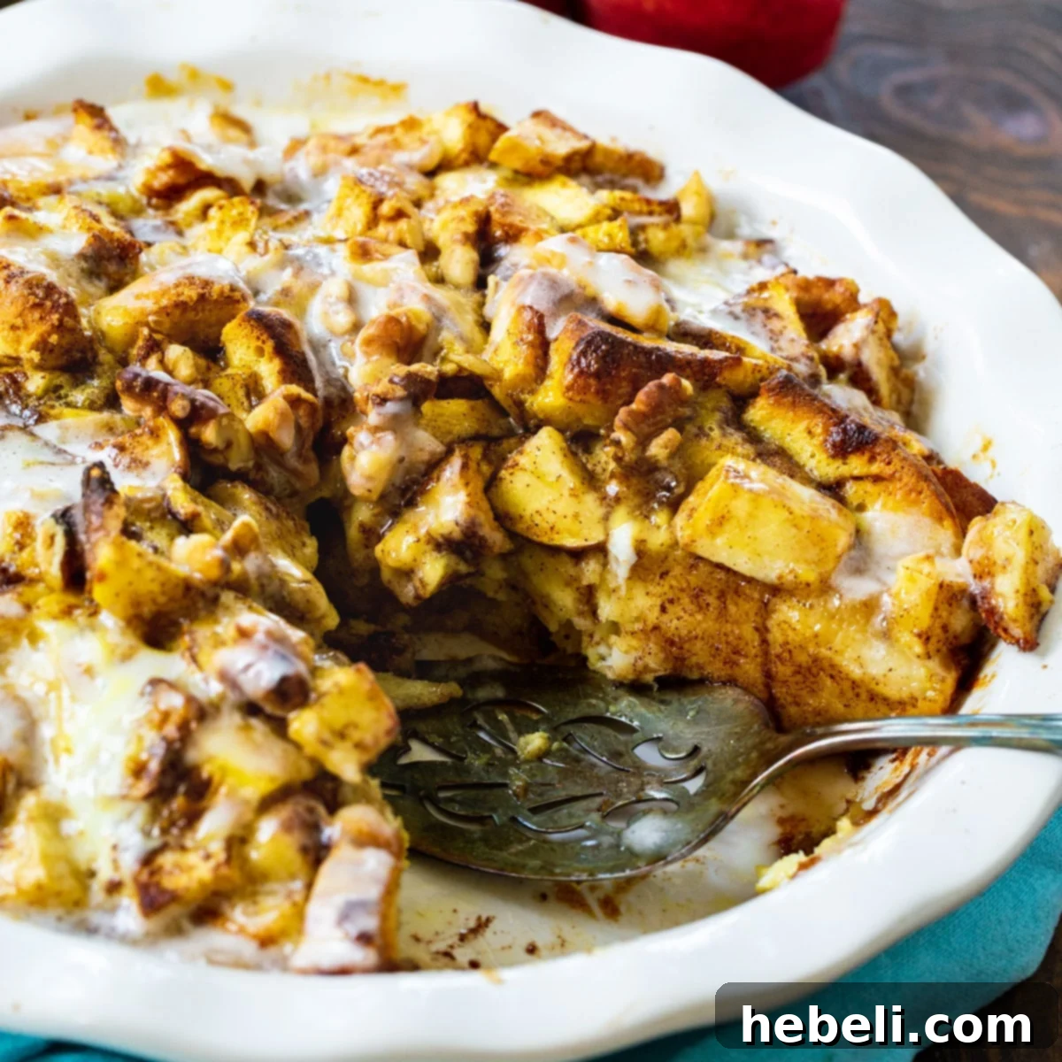 A golden-brown Apple Cinnamon Roll Bake with a slice removed, revealing gooey apples and cinnamon rolls inside.