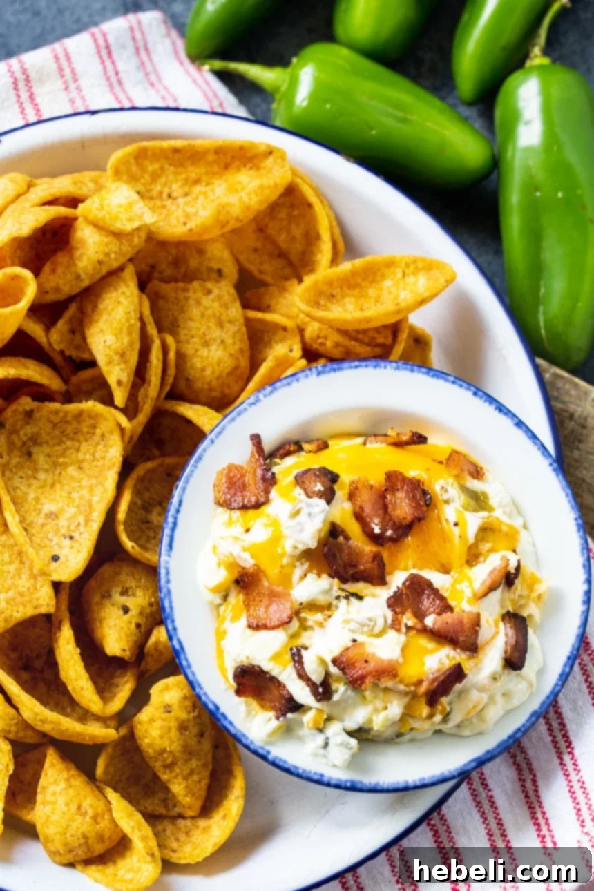 Ultimate Slow Cooker Jalapeno Popper Dip 4 A serving of creamy Slow Cooker Jalapeno Popper Dip in a small bowl, garnished with fresh cilantro, alongside a plate of crispy corn chips.