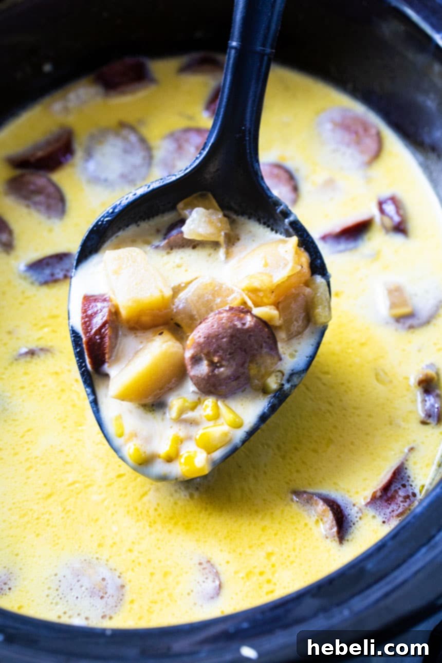 Hearty Slow Cooker Potato and Kielbasa Chowder 3 A spoon scooping a generous portion of creamy potato and kielbasa chowder from a slow cooker.