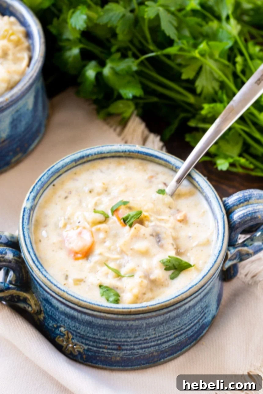 A bowl of creamy chicken wild rice soup, garnished with parsley, with fresh parsley sprigs next to it.