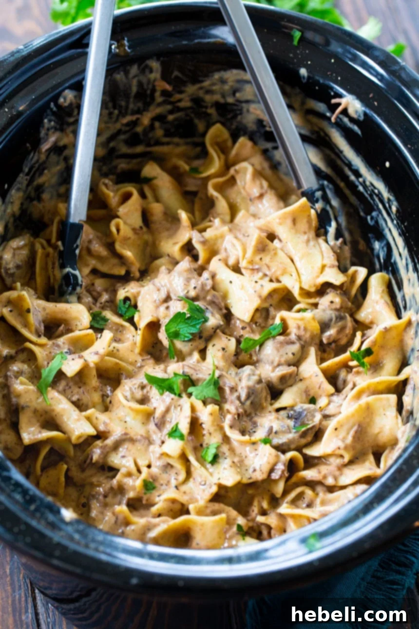 Beef Stroganoff simmering in a slow cooker with serving tongs.