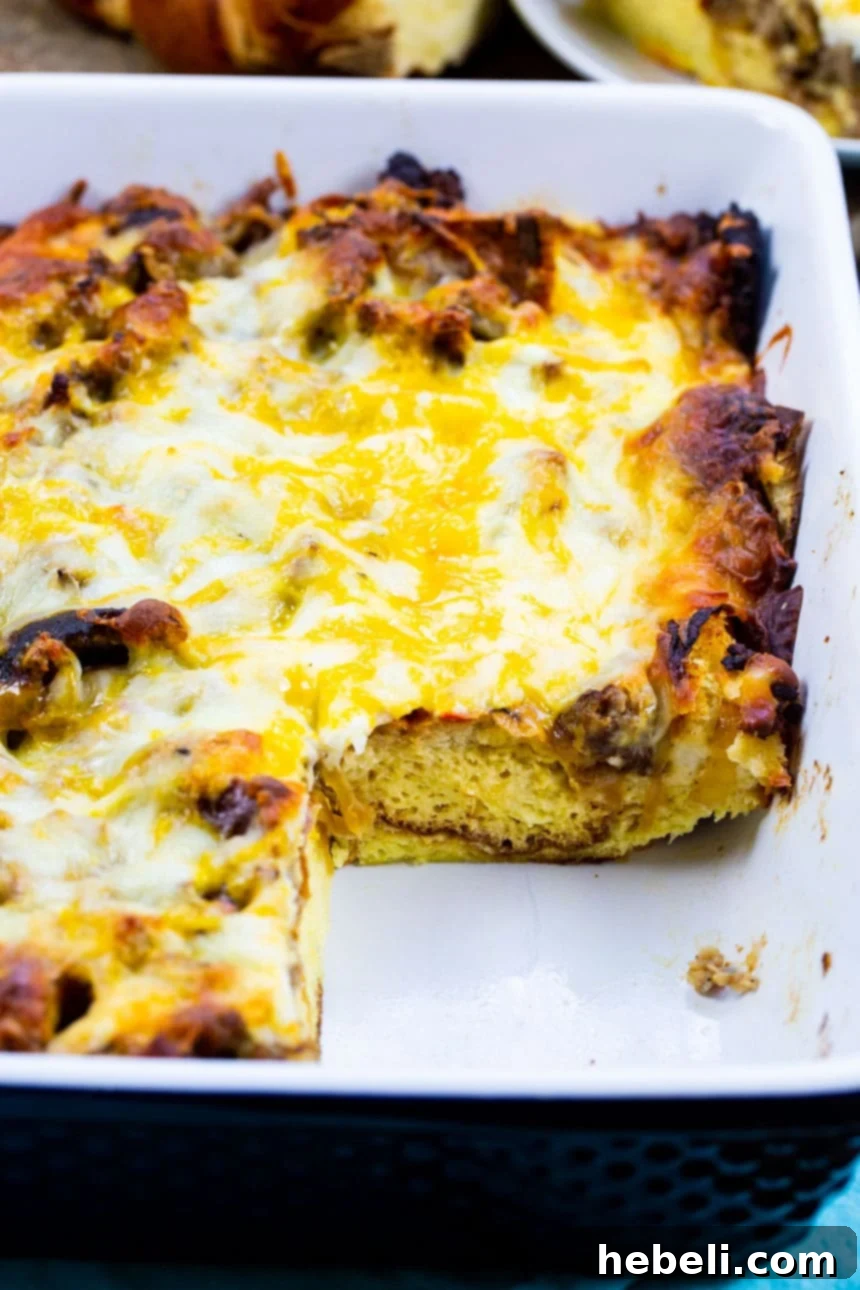 A close-up view of the baked breakfast casserole with a square slice carefully removed, revealing the delicious layers of bread, sausage, caramelized onions, and melted cheese inside.