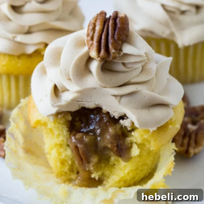 A Pecan Pie Cupcake with a bite taken out, clearly showing the gooey pecan pie filling inside, topped with fluffy buttercream.
