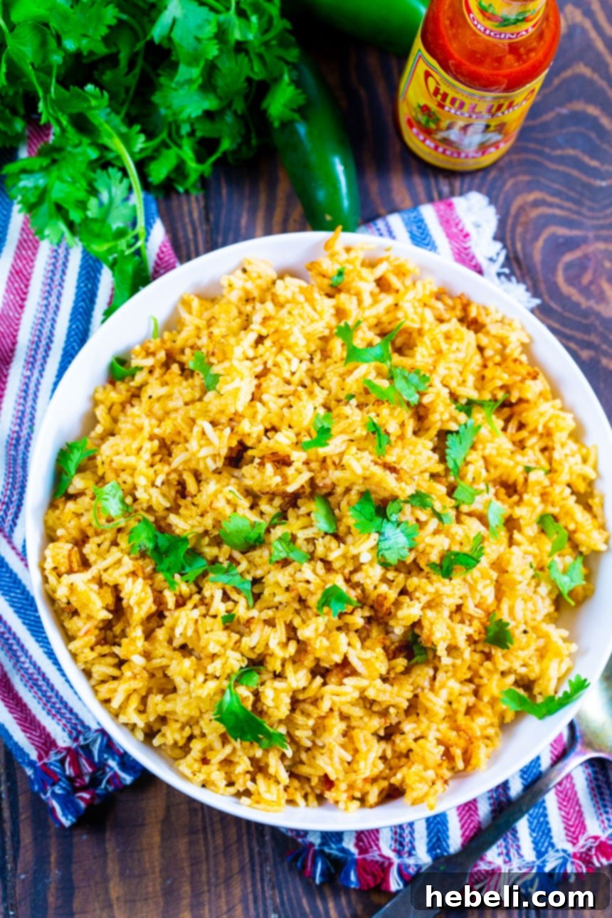 Overhead shot of Perfect Mexican Rice in a bowl with a bottle of hot sauce and fresh cilantro, highlighting the garnish.
