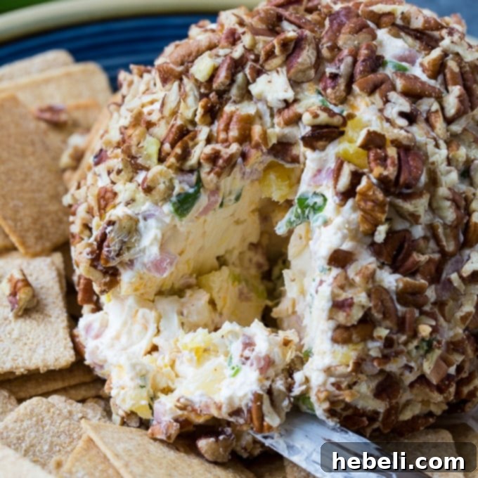 A festive Ham and Pineapple Cheese Ball on a plate with an assortment of crackers.