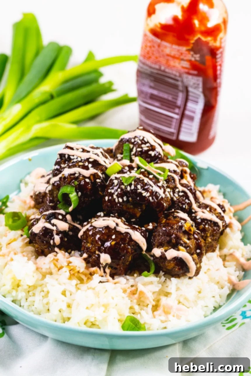 Effortless Korean Bulgogi Meatballs 3 Close-up of Beef Bulgogi Meatballs served over rice, generously drizzled with a creamy Sriracha sauce and garnished with fresh green onions.
