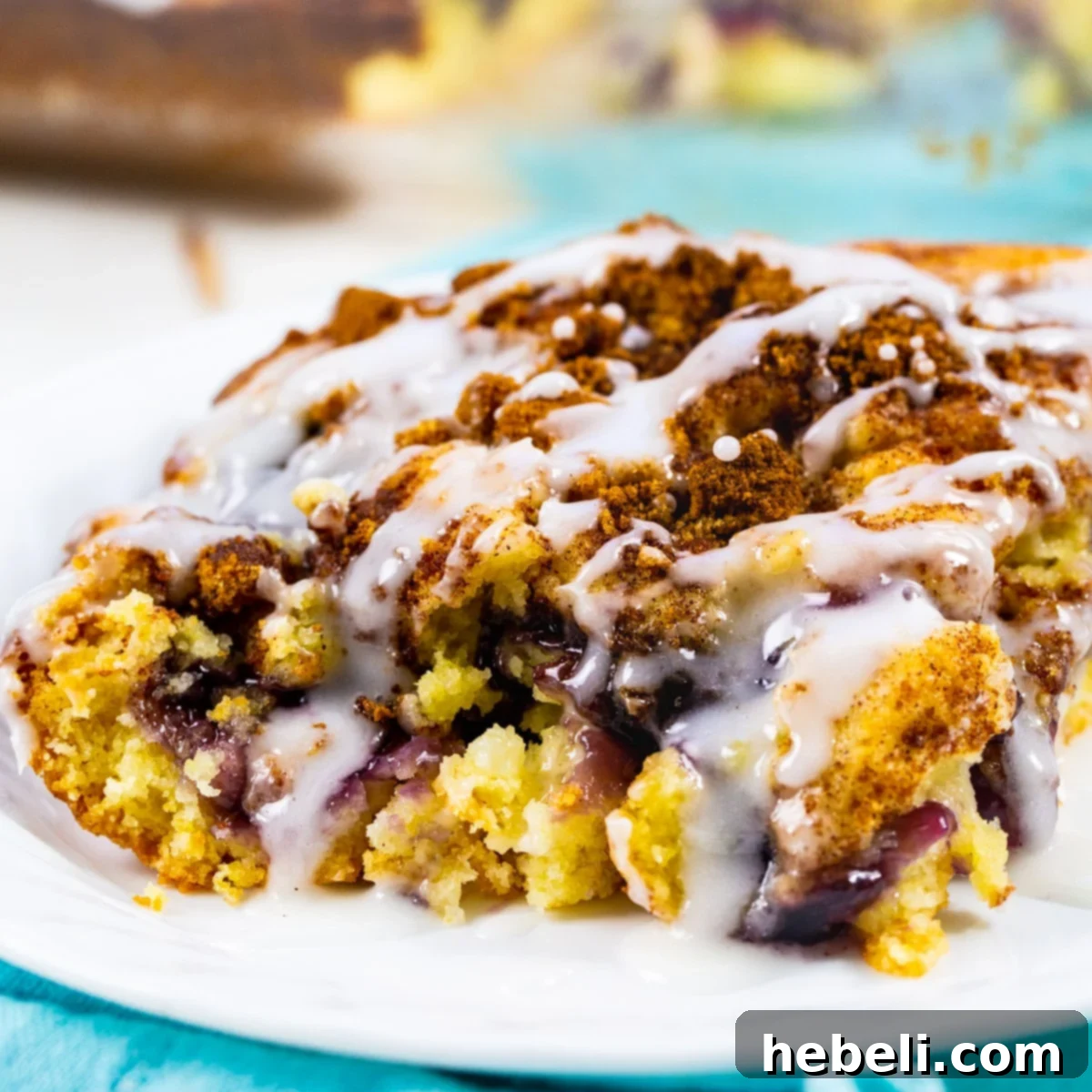 Blueberry Pie Coffee Cake Perfection 2 Slice of luscious Blueberry Pie Coffee Cake on a pristine white plate, showcasing its moist texture and vibrant blueberry filling, topped with a sweet glaze.