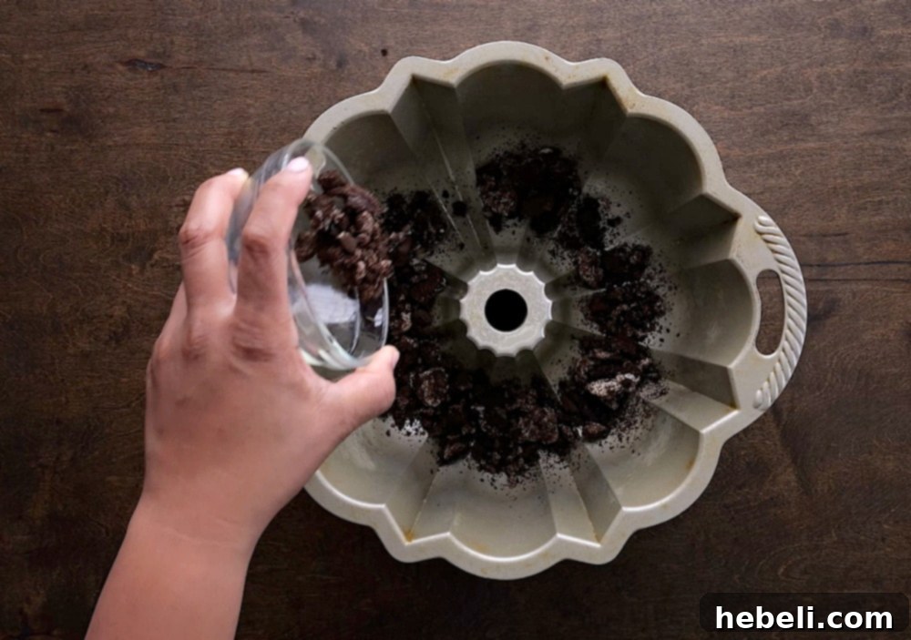 Oreo crumbs generously sprinkled into a greased bundt pan, forming the base of the monkey bread.