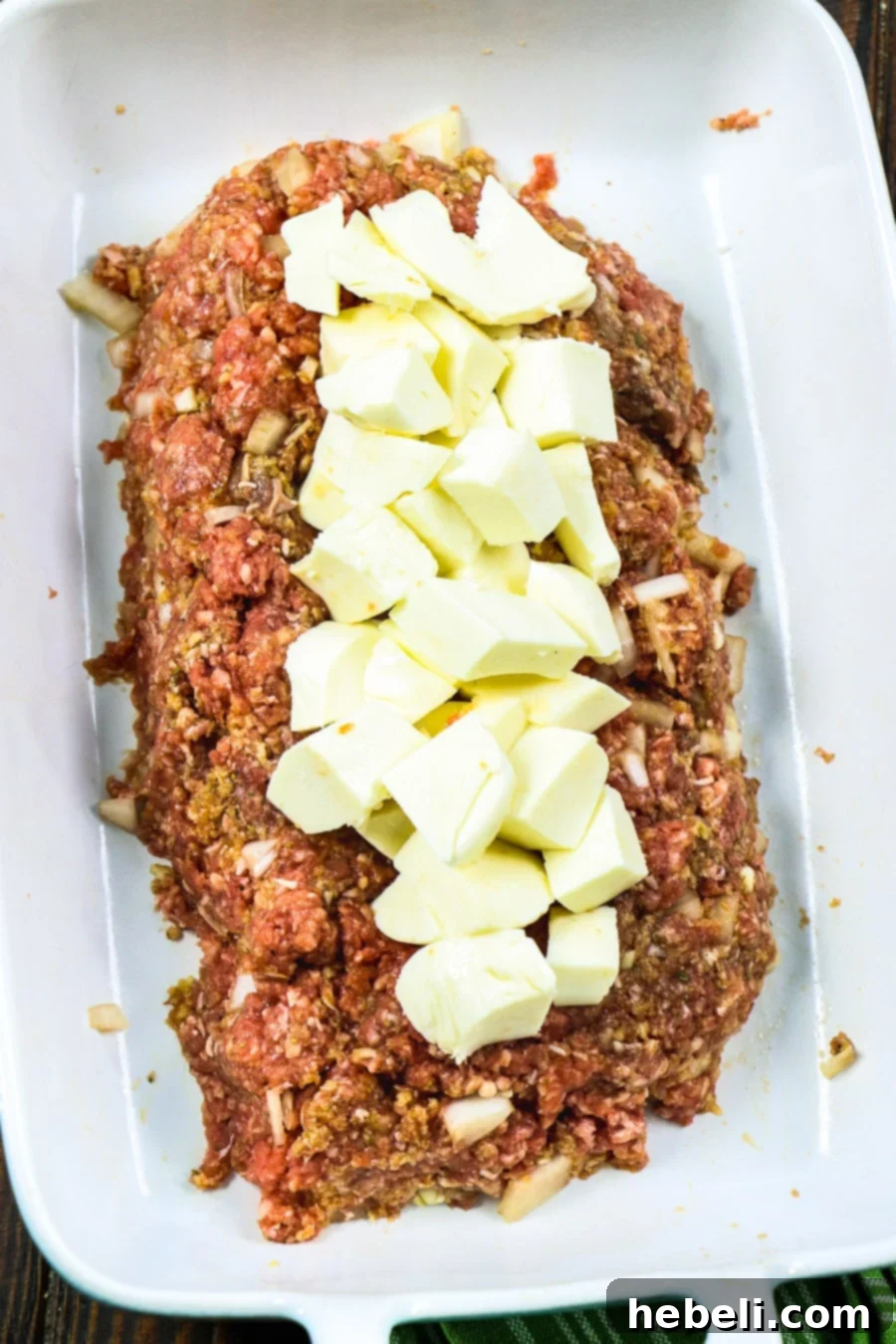 Diced mozzarella cheese being placed onto the ground beef mixture for stuffing.