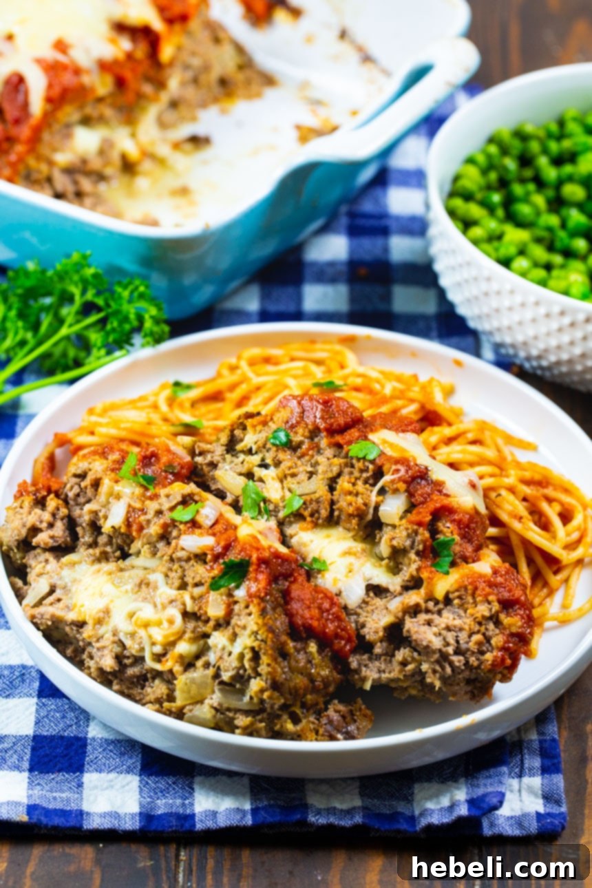 Beautifully sliced Mozzarella Stuffed Meatloaf on a plate, revealing the melted cheese, served with pasta.