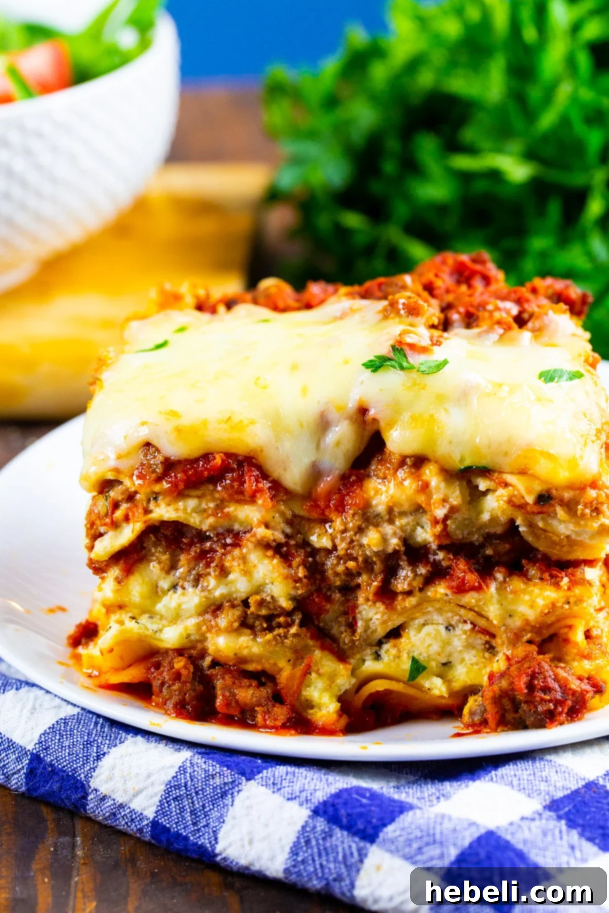 A generous slice of slow cooker sausage lasagna, showing distinct layers of pasta, meat sauce, and cheese, served on a white plate.