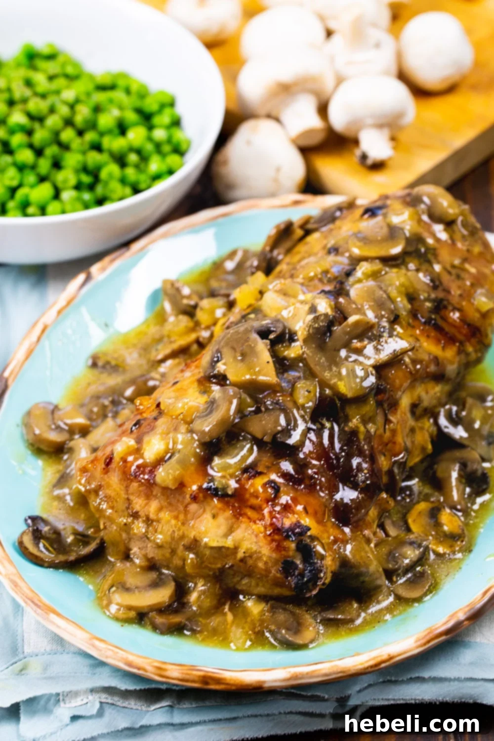Plated Roasted Pork Loin with Creamy Mushroom Gravy, expertly sliced, served alongside a vibrant bowl of green peas, presenting a complete and appealing family meal.