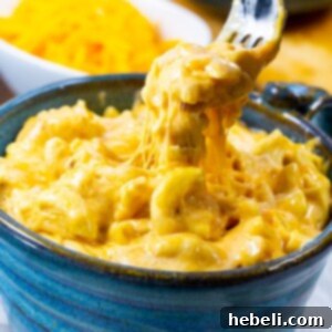 A vibrant close-up of a fork lifting a gooey spoonful of Slow Cooker Ultra Creamy Mac and Cheese.