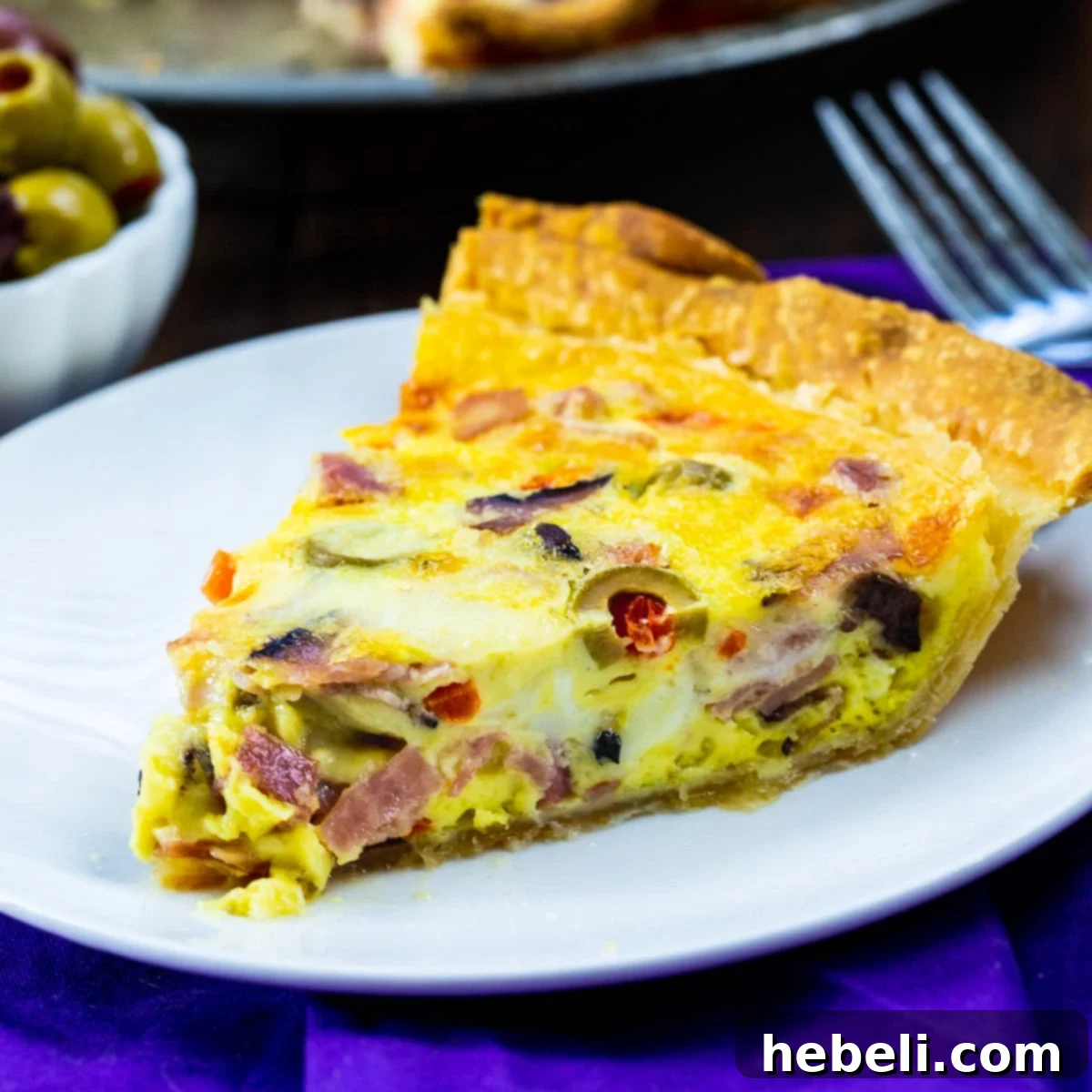 Savory Muffaletta Quiche 2 Slice of Muffaletta Quiche on a white plate, showcasing olives, meats, and cheese with a golden crust.