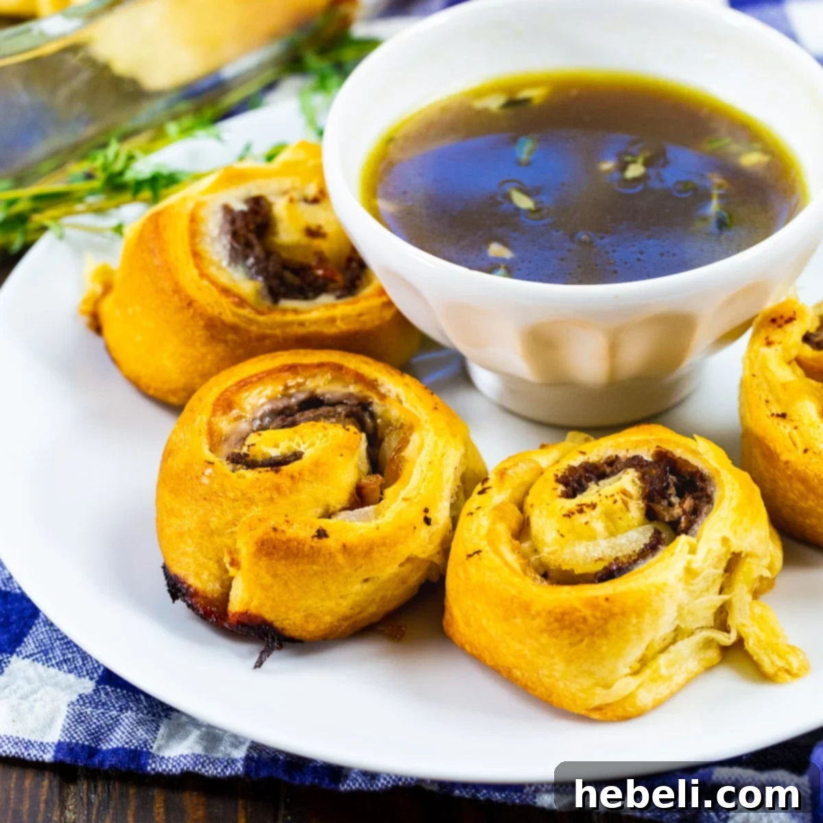 Flavorful French Dip Roll-Ups 2 Golden-baked French Dip Pinwheels arranged on a plate with a small bowl of savory Au Jus for dipping.