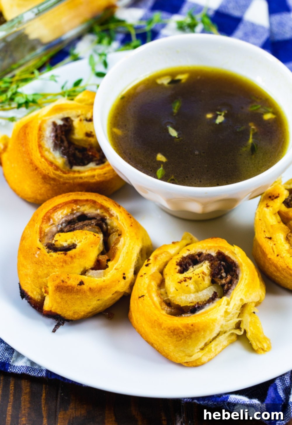 Flavorful French Dip Roll-Ups 5 Freshly baked French Dip Pinwheels on a white plate, accompanied by a small ramekin of rich Au Jus for dipping.