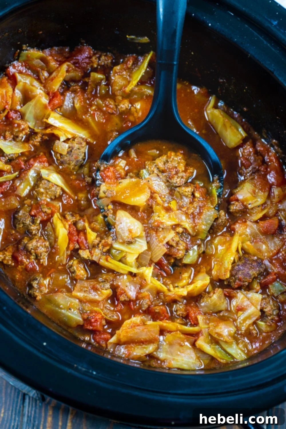 A large serving spoon scooping a portion of Slow Cooker Spicy Cabbage Beef Soup, highlighting the generous chunks of beef and tender cabbage.