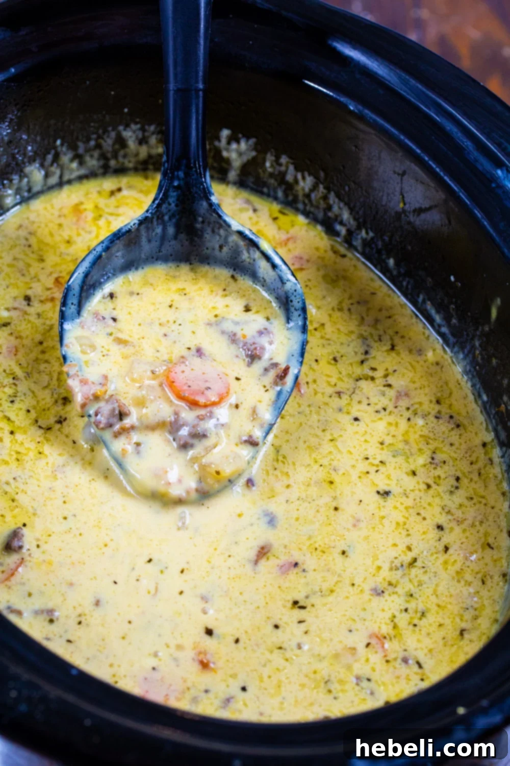 Loaded Slow Cooker Bacon Cheeseburger Soup 3 A close-up of creamy Slow Cooker Bacon Cheeseburger Soup simmering gently in a red crockpot, emitting steam.