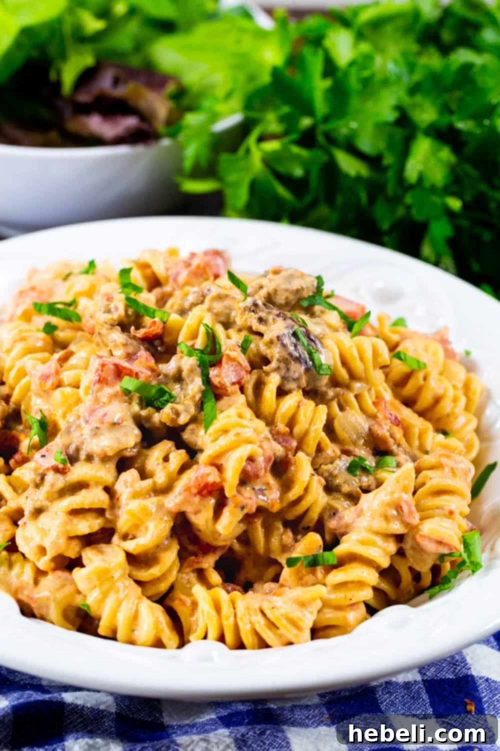 Close-up of Creamy Rotel Pasta with Sausage in a white bowl with a spoon, garnished with parsley.