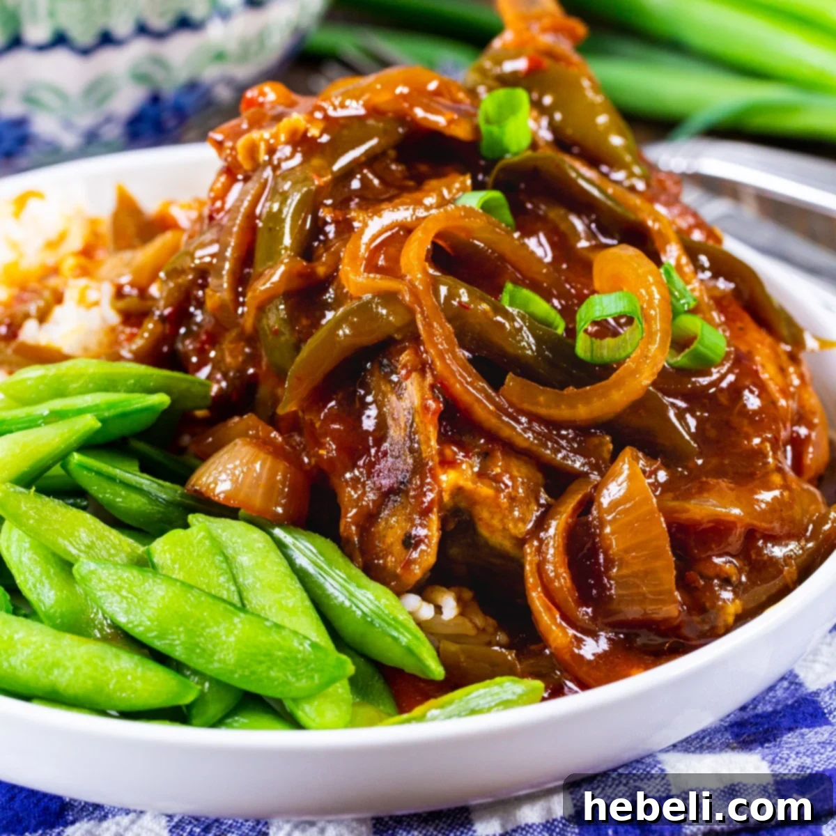 A beautifully plated dish of Slow Cooker Sweet and Tangy Asian Pork Chops with sugar snap peas, garnished with green onions.