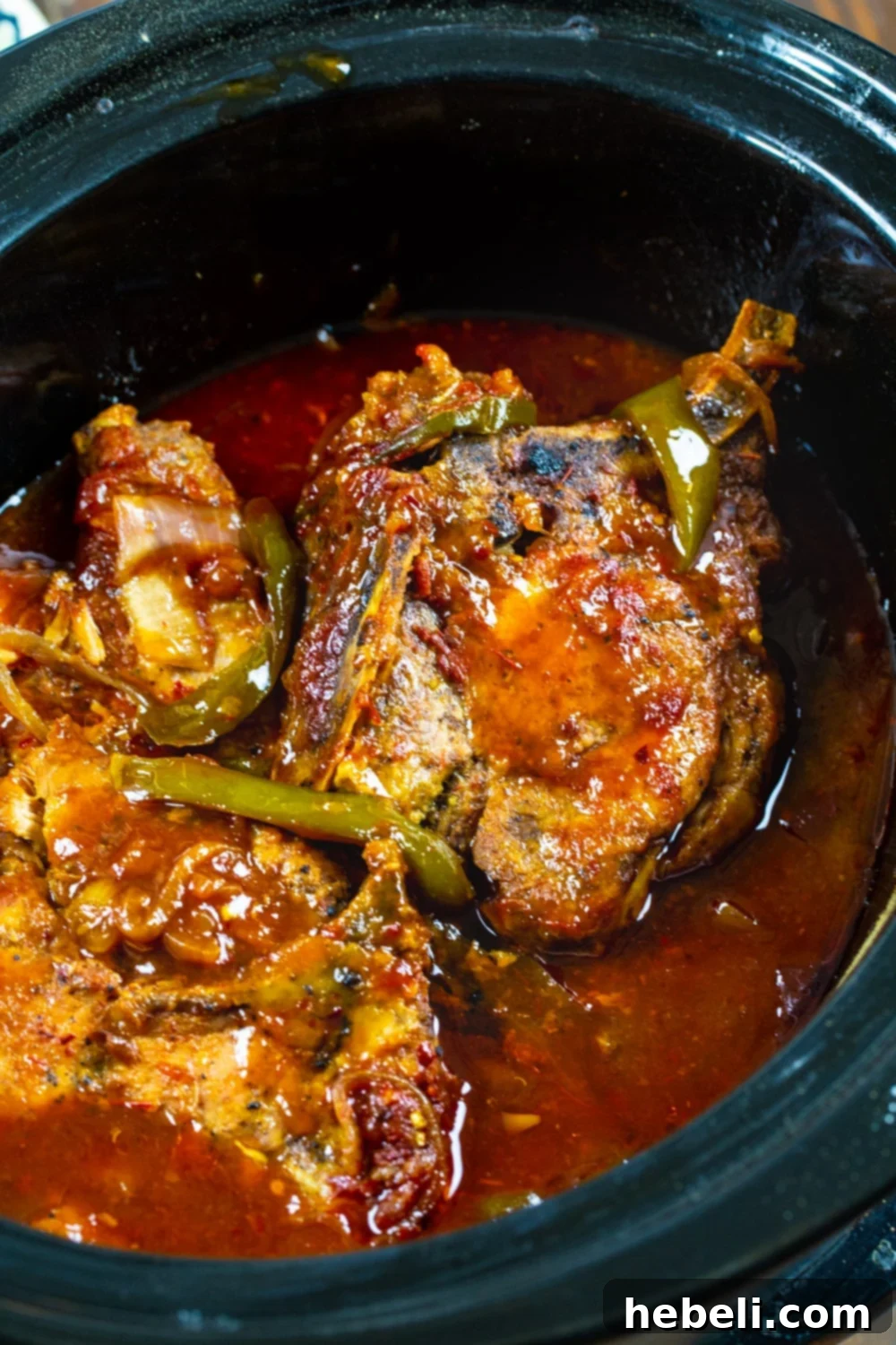 Asian Pork Chops cooking in a slow cooker, submerged in a sweet and tangy sauce with onions and bell peppers.