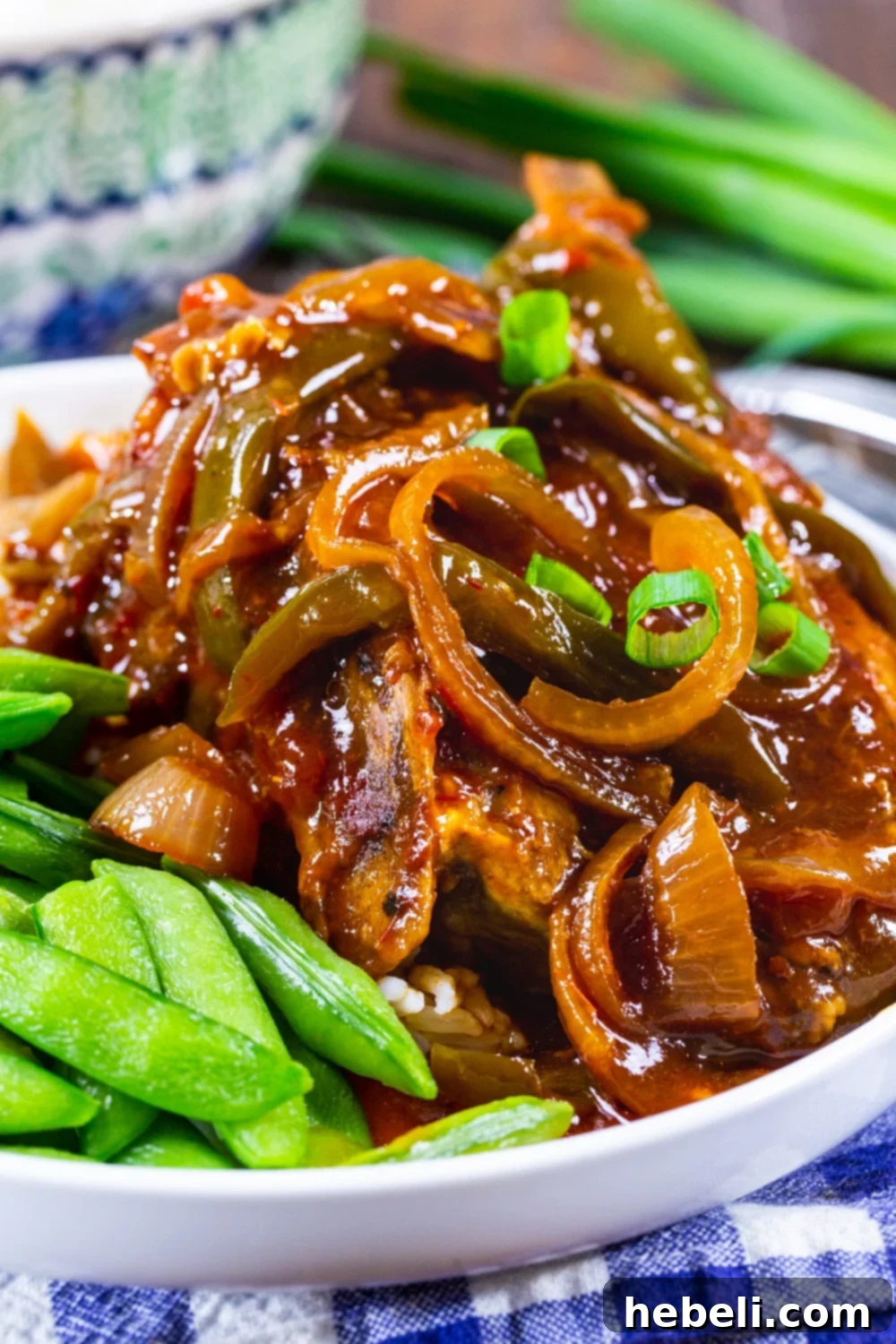 Close-up of a serving of Slow Cooker Sweet and Tangy Asian Pork Chops on a white plate, garnished with green onions and sugar snap peas.