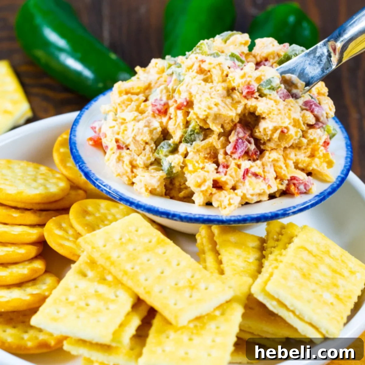 A beautifully presented bowl of creamy Roasted Jalapeno Pimento Cheese, generously garnished and surrounded by an assortment of crisp crackers and fresh vegetable sticks, inviting a delicious tasting experience.