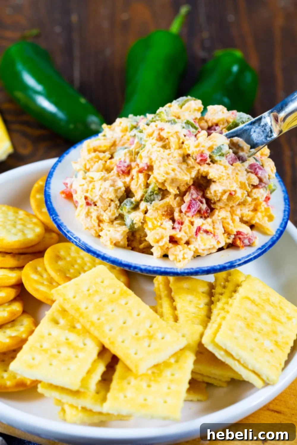 A close-up shot of creamy Pimento Cheese served in a small elegant white bowl, delicately placed on a decorative plate and surrounded by an array of gourmet crackers, ready for an appetizer spread.