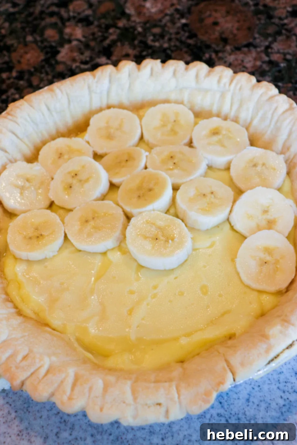 Creamy Chocolate Banana Bliss 3 Freshly sliced bananas being arranged neatly on top of the first layer of banana cream pudding in a pie crust.
