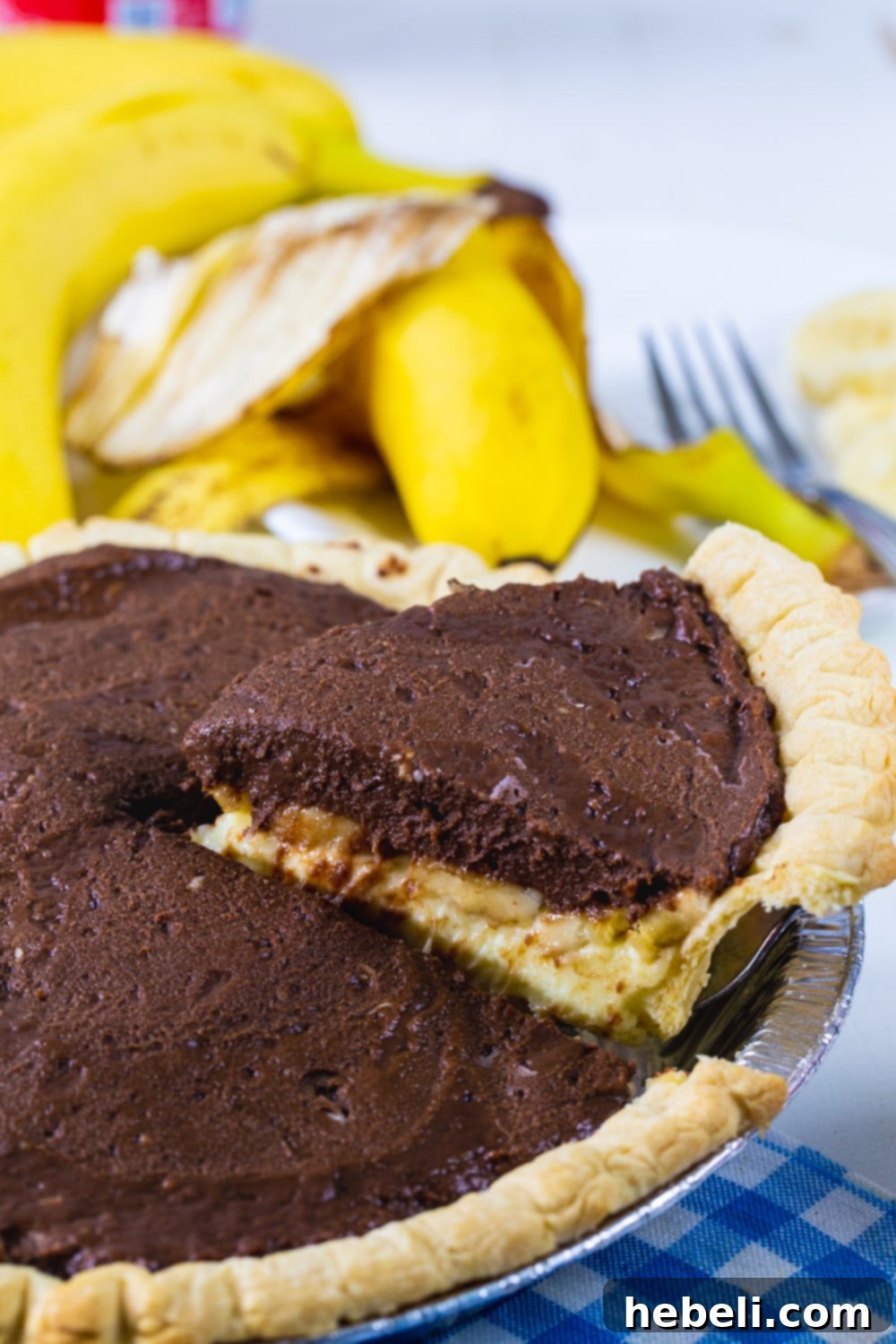 Creamy Chocolate Banana Bliss 4 A whole Chocolate Banana Cream Pie with one slice carefully being lifted out of the pie dish, showing the distinct layers of banana and chocolate.