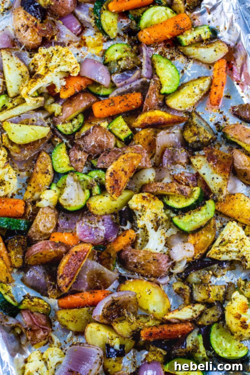 A close-up shot of seasoned Italian Roasted Vegetables spread out evenly on a baking sheet, showcasing their vibrant colors and crispy edges as they roast in the oven.