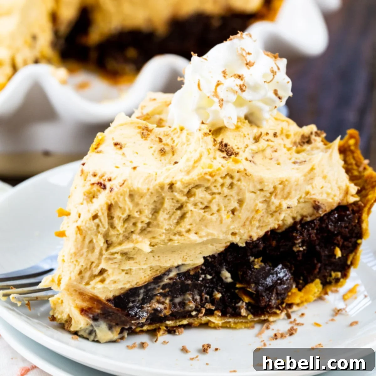 A perfectly sliced piece of Peanut Butter Mousse Brownie Pie on an elegant white plate, showcasing its distinct layers of golden crust, dark brownie, and fluffy peanut butter mousse, ready to be enjoyed.