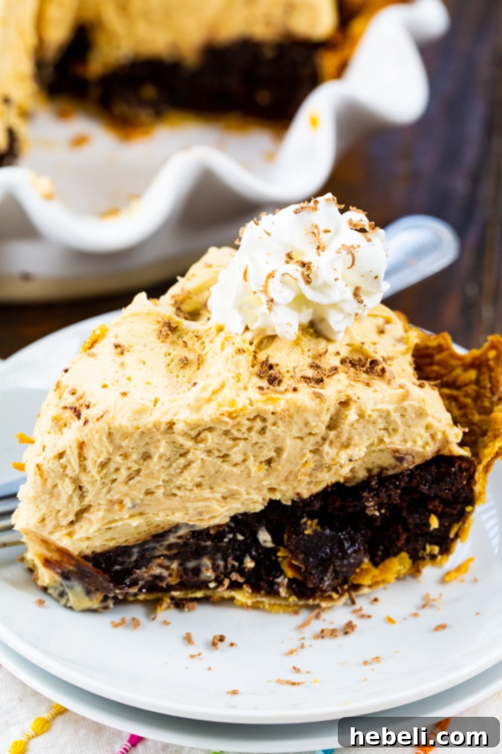 A close-up view of a slice of Peanut Butter Mousse Brownie Pie, generously topped with fluffy whipped cream, resting on a white plate with a fork beside it, inviting a delicious bite.