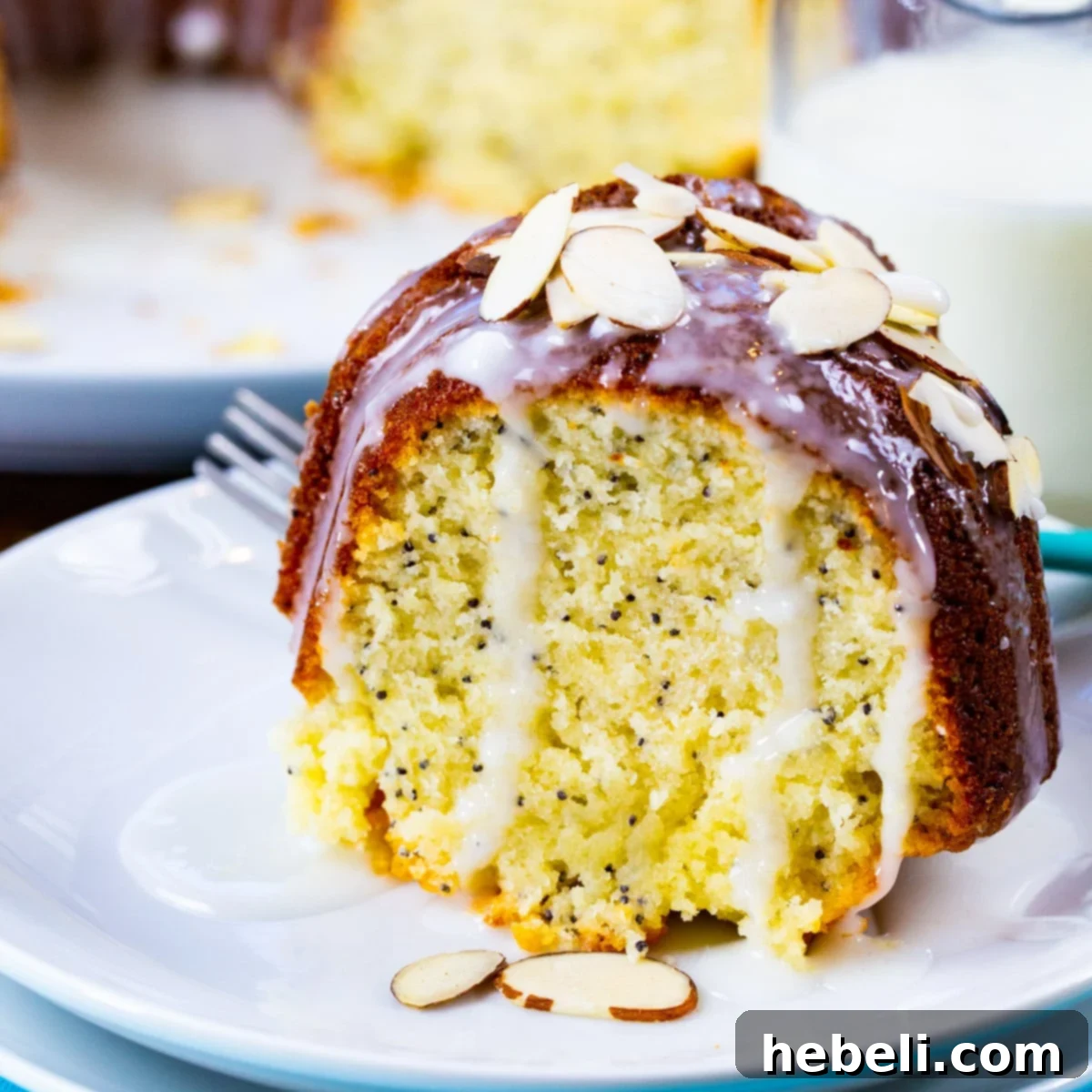 A perfectly sliced piece of Almond Poppy Seed Pound Cake on a white plate, showcasing its moist crumb and glossy almond glaze.