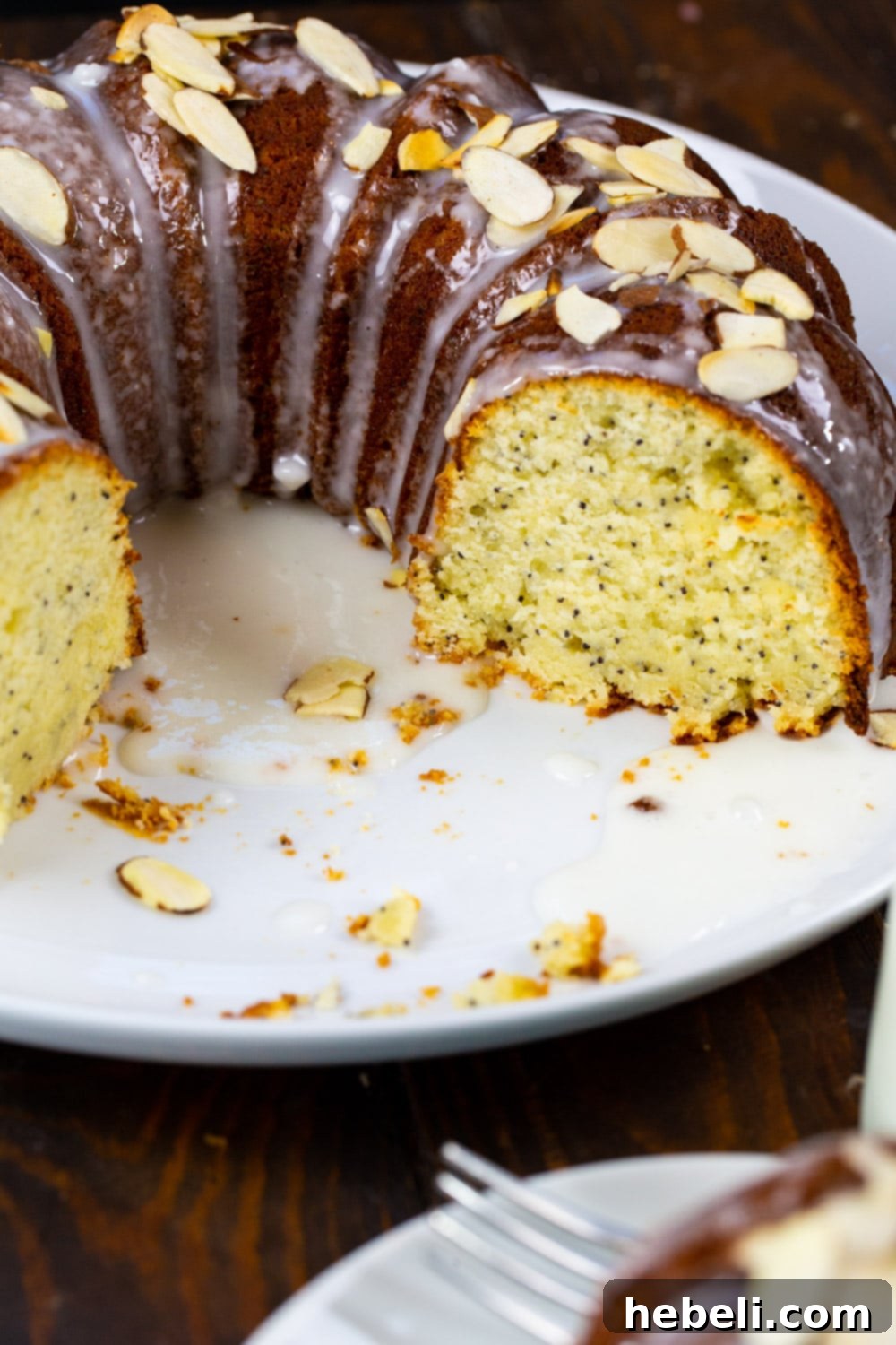 A beautifully glazed Almond Poppy Seed Pound Cake with several slices already cut, revealing the intricate bundt pattern and poppy seeds within.