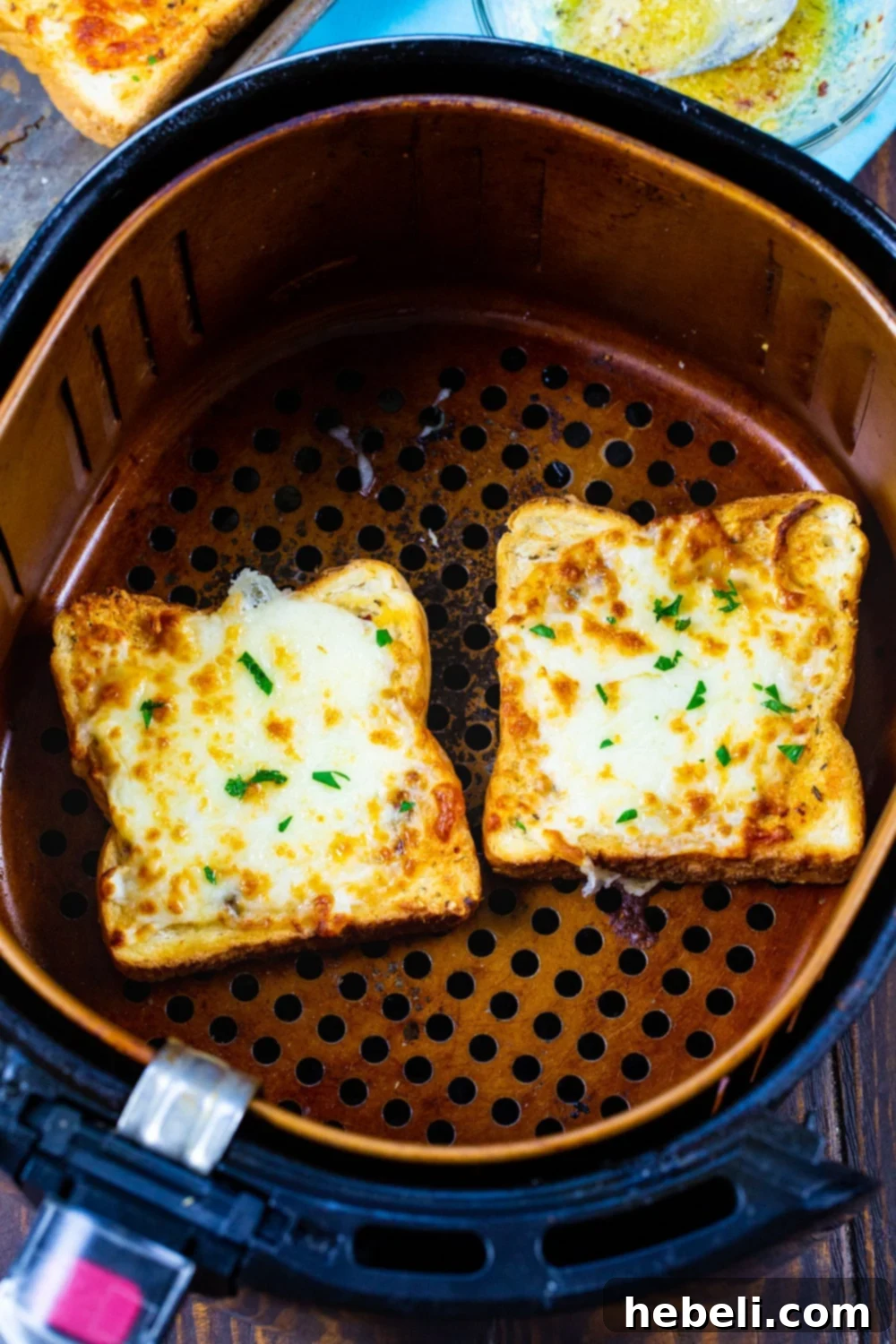 Two slices of Texas Toast prepared for air frying, with butter and cheese, inside an air fryer basket.