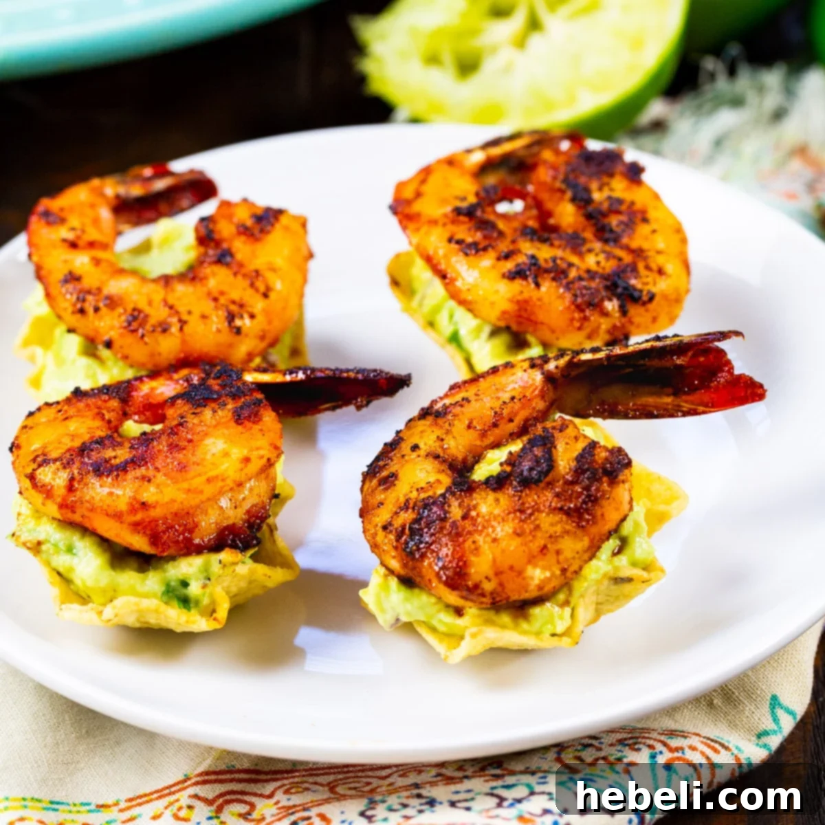 A plate featuring four perfectly assembled Shrimp Tostada Bites, showcasing the vibrant green guacamole and succulent pink shrimp.