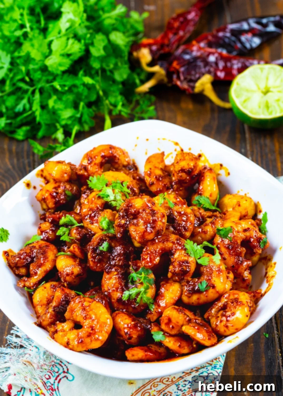 Plump, red Chile and Garlic Shrimp nestled in a bowl, with fresh green cilantro leaves scattered beside it, highlighting the vibrant colors and fresh ingredients.