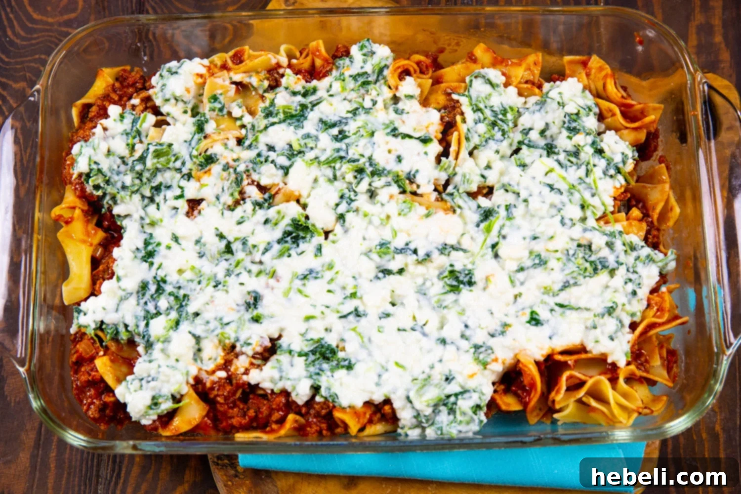 A layer of creamy cottage cheese and spinach mixture spread over egg noodles and meat sauce in a baking dish, ready for the next layer of cheese.