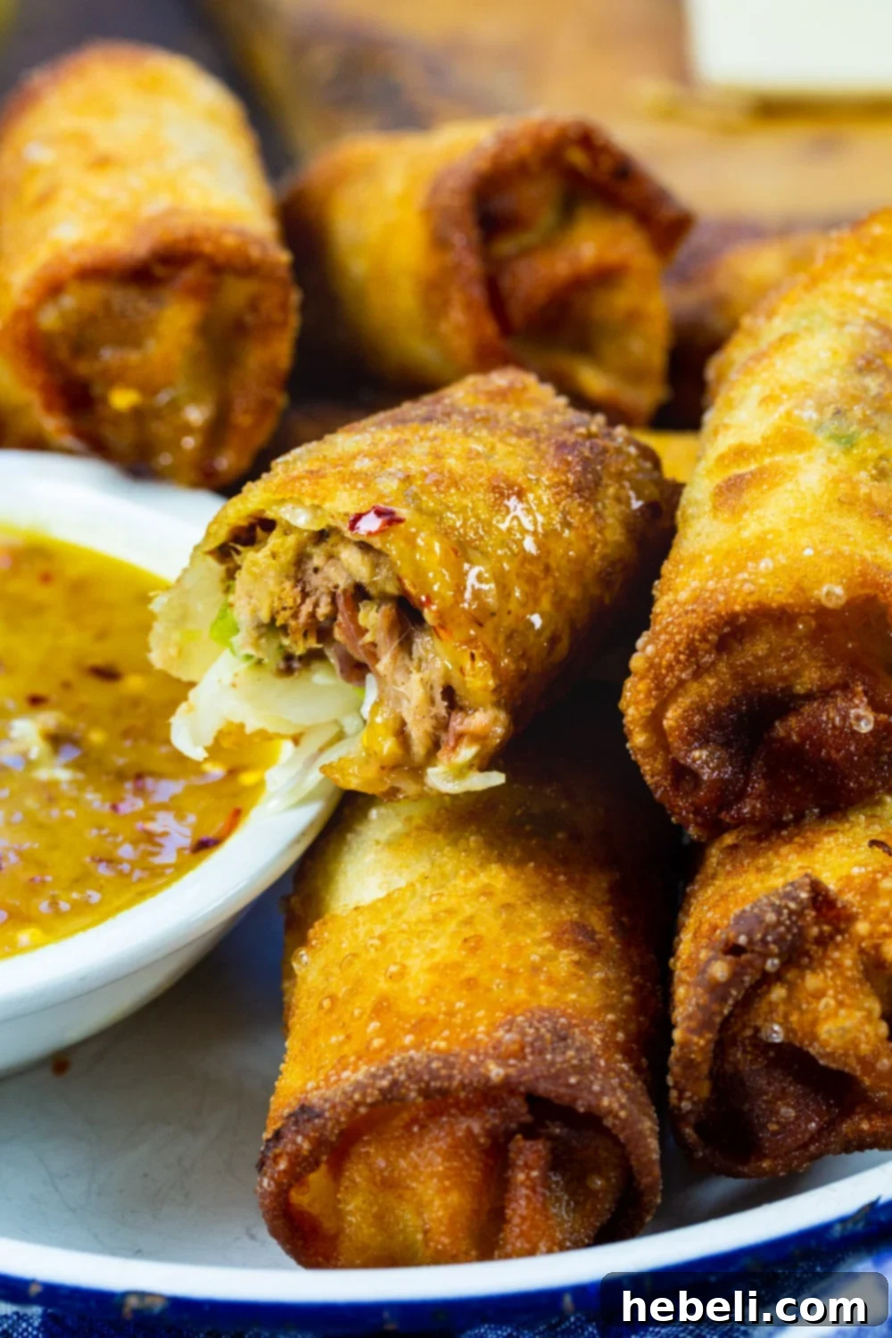 Smoky BBQ Pork Egg Rolls 6 A golden-brown Pulled Pork Egg Roll being dipped into a small bowl of tangy peach dipping sauce, highlighting its crispy texture.