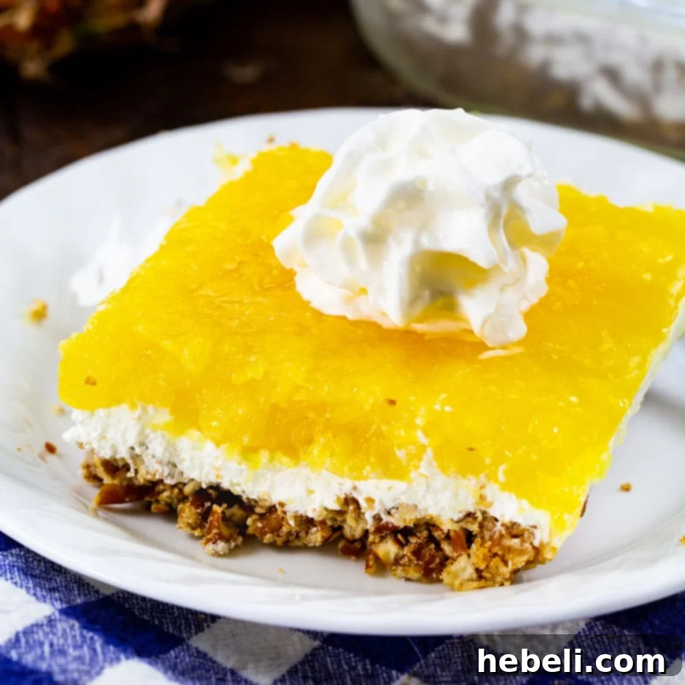 A square serving of Pineapple Pretzel Salad on a white plate, showcasing its distinct layers.