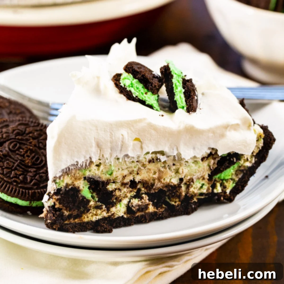 A perfectly sliced piece of No-Bake Mint Oreo Pie on a white plate, showcasing its creamy mint filling and Oreo crust.