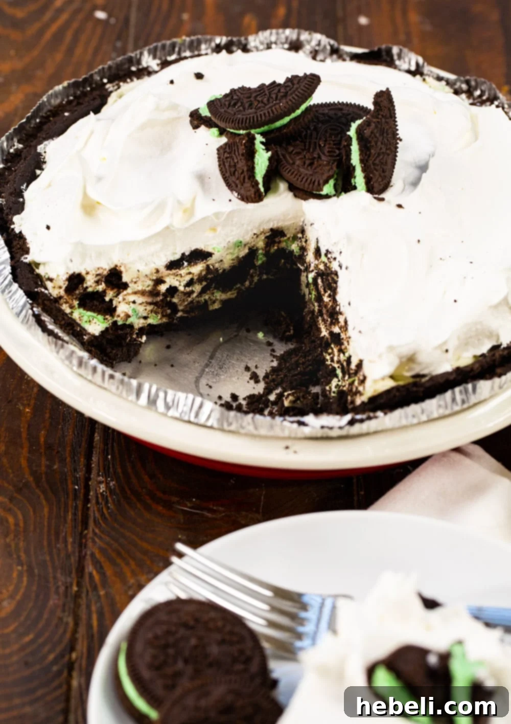 Close-up shot of a whole No-Bake Mint Oreo Pie with a slice removed, revealing the green mint filling and dark Oreo crust.