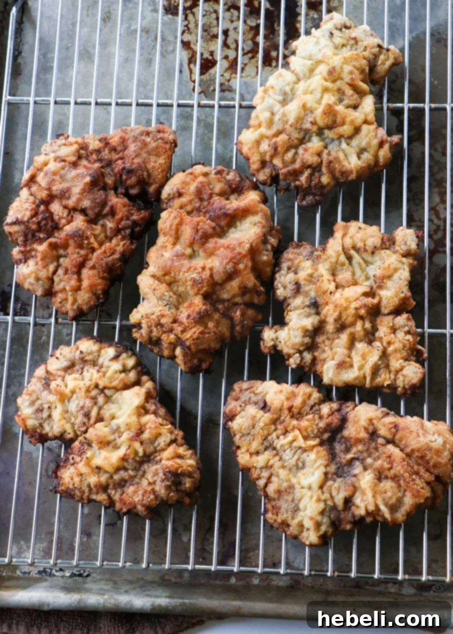 Golden-brown, perfectly fried cubed steak pieces resting on a wire rack after cooking, ready for gravy.